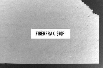 A rectangular piece of material labeled "FIBERFRAX 970F" with a slightly torn upper right corner, set against a dark background.