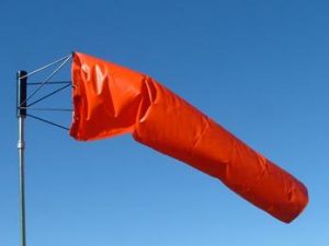 A bright orange windsock extends horizontally against a clear blue sky, indicating strong wind.