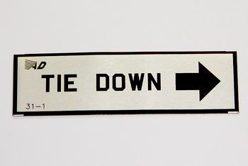 Sign with bold text "TIE DOWN" and a large black arrow pointing right on a white background.